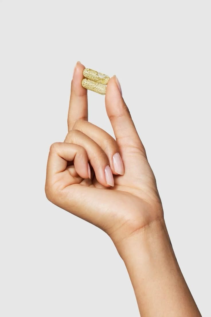 A hand holding two unbranded wellness capsules